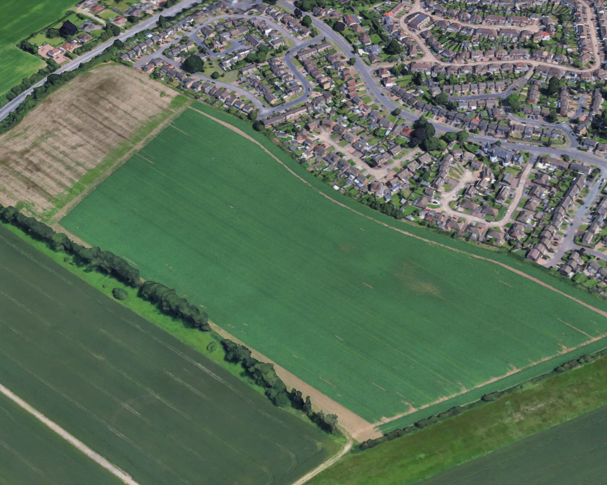 Aerial view of a large green field surrounded by roads and an existing housing estate.